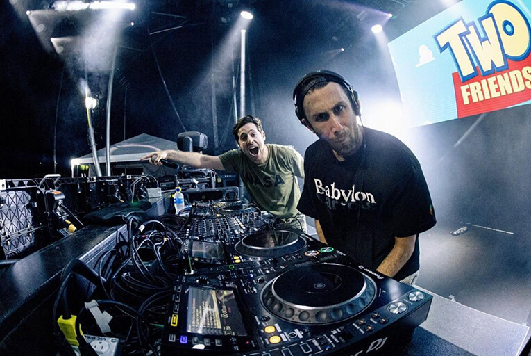 Two Friends looking at the camera from behind their DJ controllers.