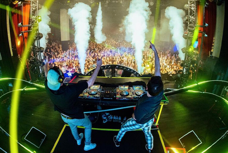 Two Friends looking at a large crowd, getting them hyped up as fog jets go off.
