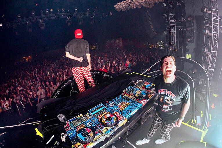 Two Friends performing in front of a large crowd. One is looking at the crowd, the other is looking at the camera.